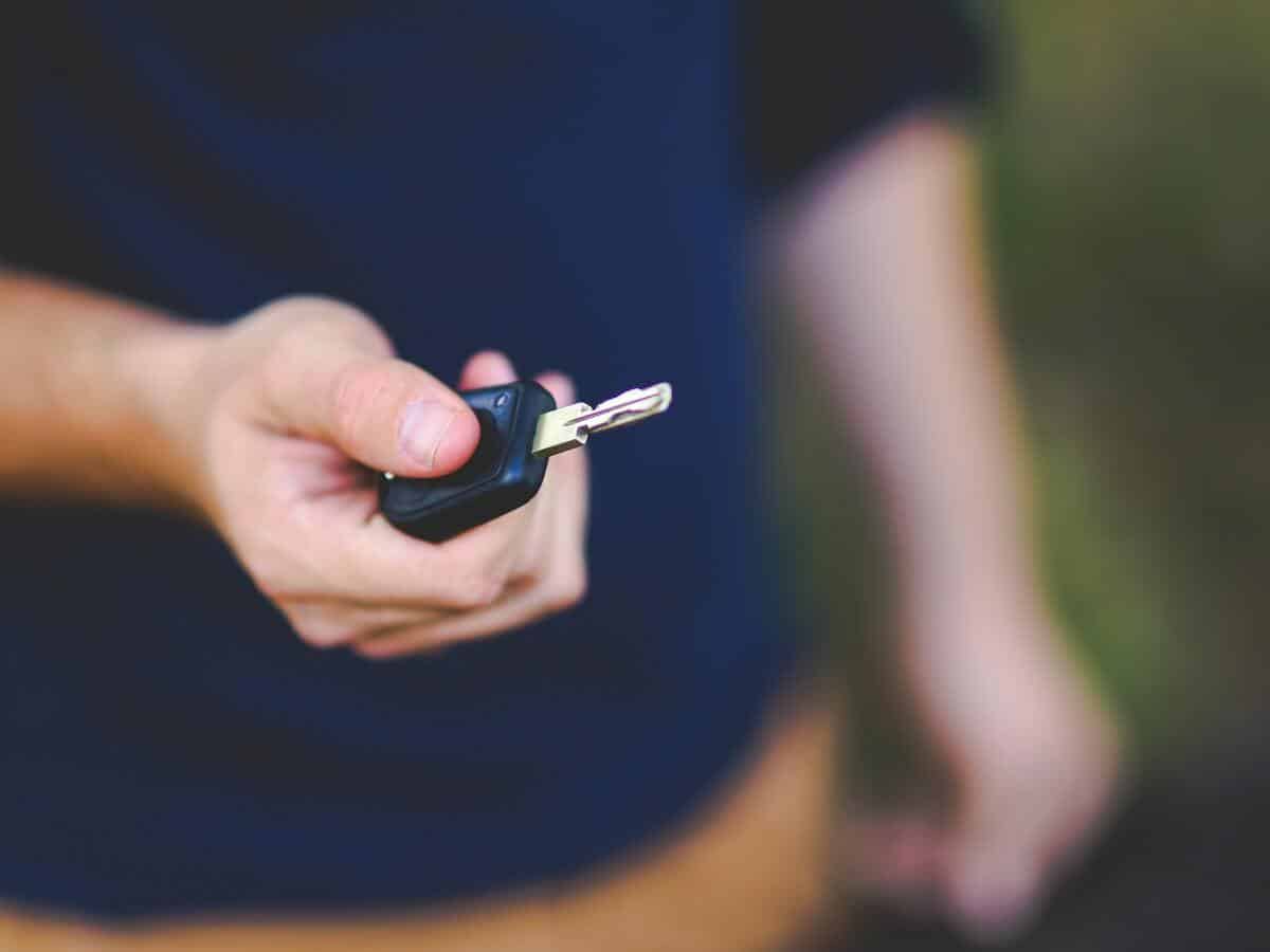 A man holding out a key to his car.