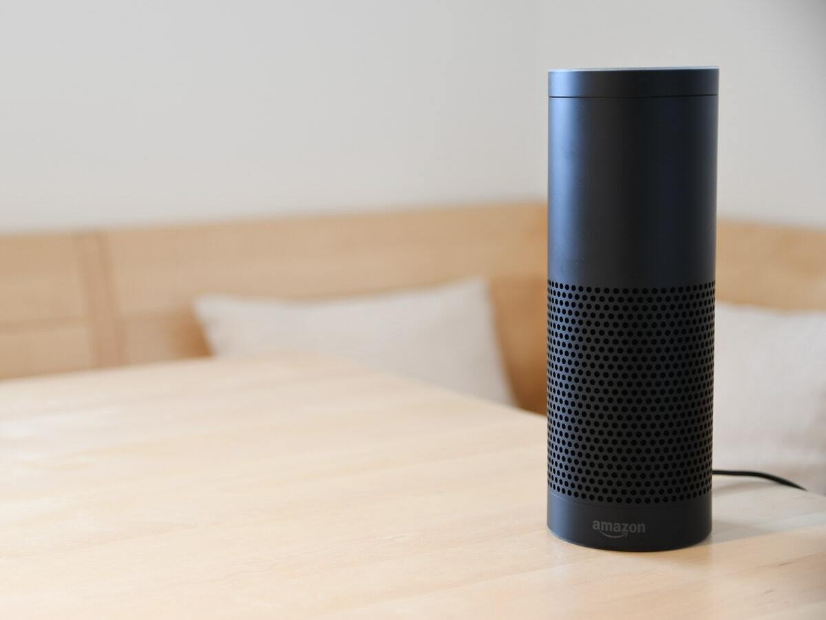 A black Amazon smart speaker sitting on a shiny wooden table.