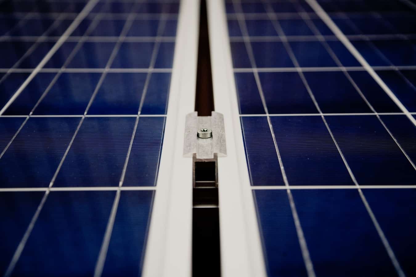 A closeup of dark blue solar panels and a white mounting component between the grids.