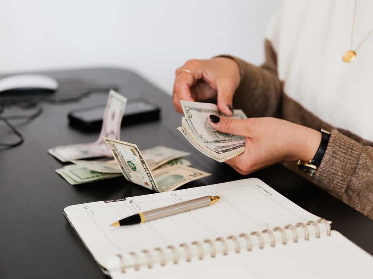 A woman counting through money on a black table that also holds her planner and cell phone.