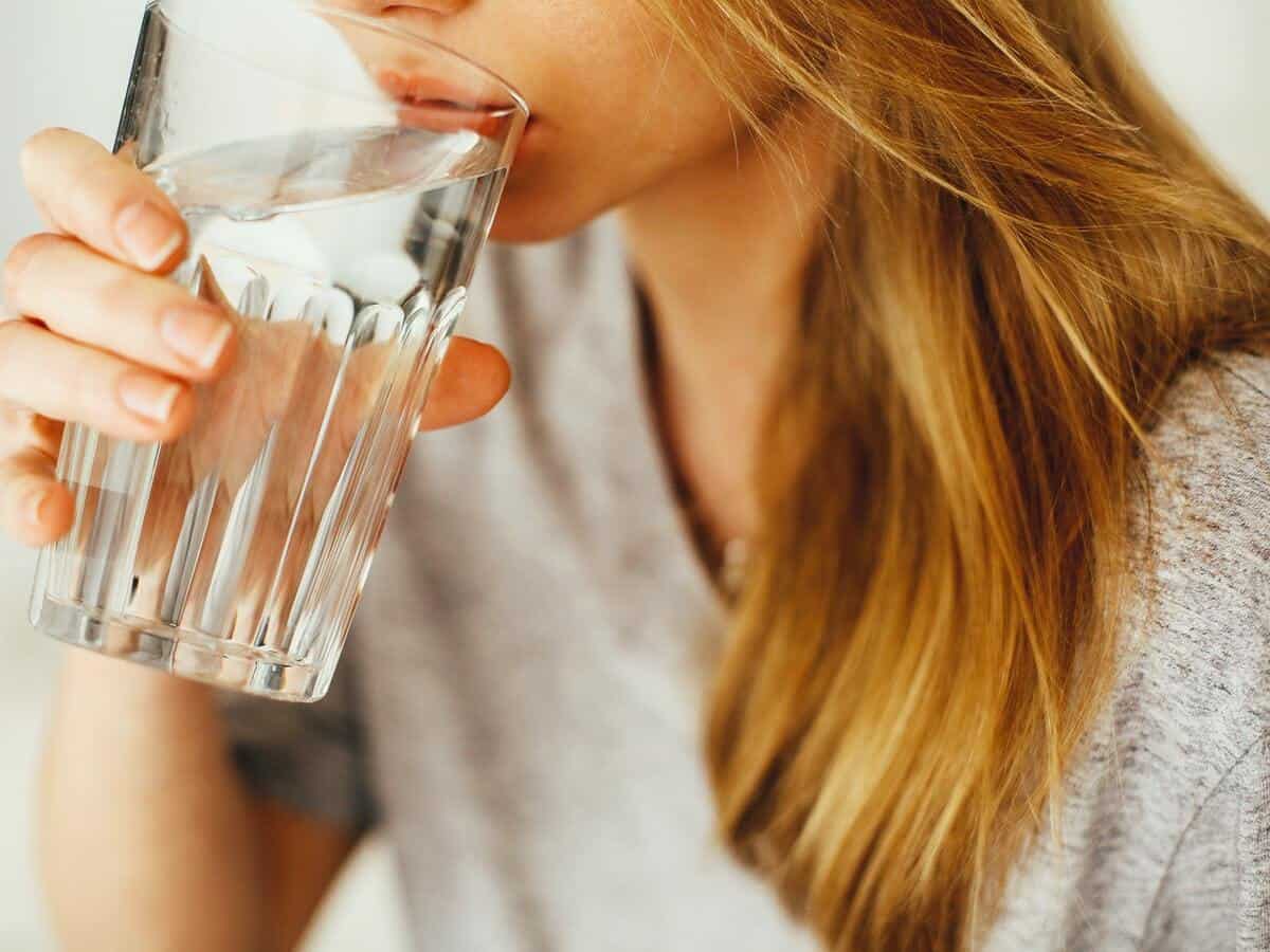 A blond woman is drinking water from a glass cup.