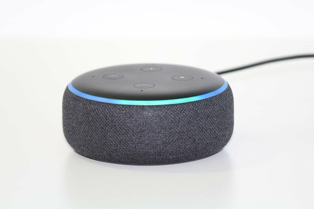 A black Amazon Echo Dot with a lit up blue ring sits on a white background.