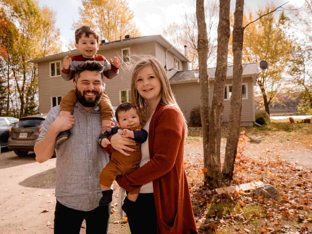 A young family of four stands outside of their two-story home.