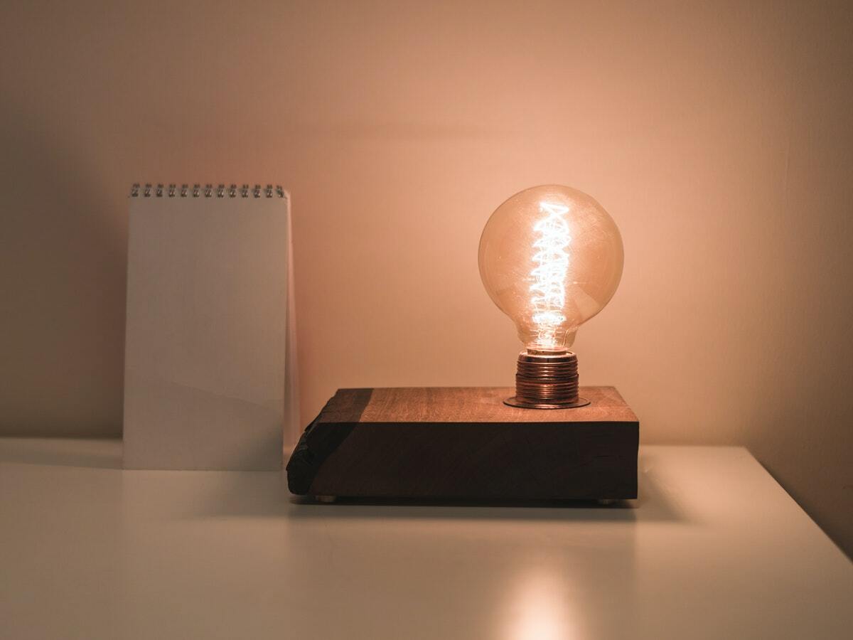 A glowing bulb attached to a light fixture sits on top of a tidy, white desk.