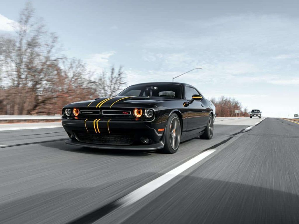 A black Dodge Challenger driving down a road on an Autumn day.