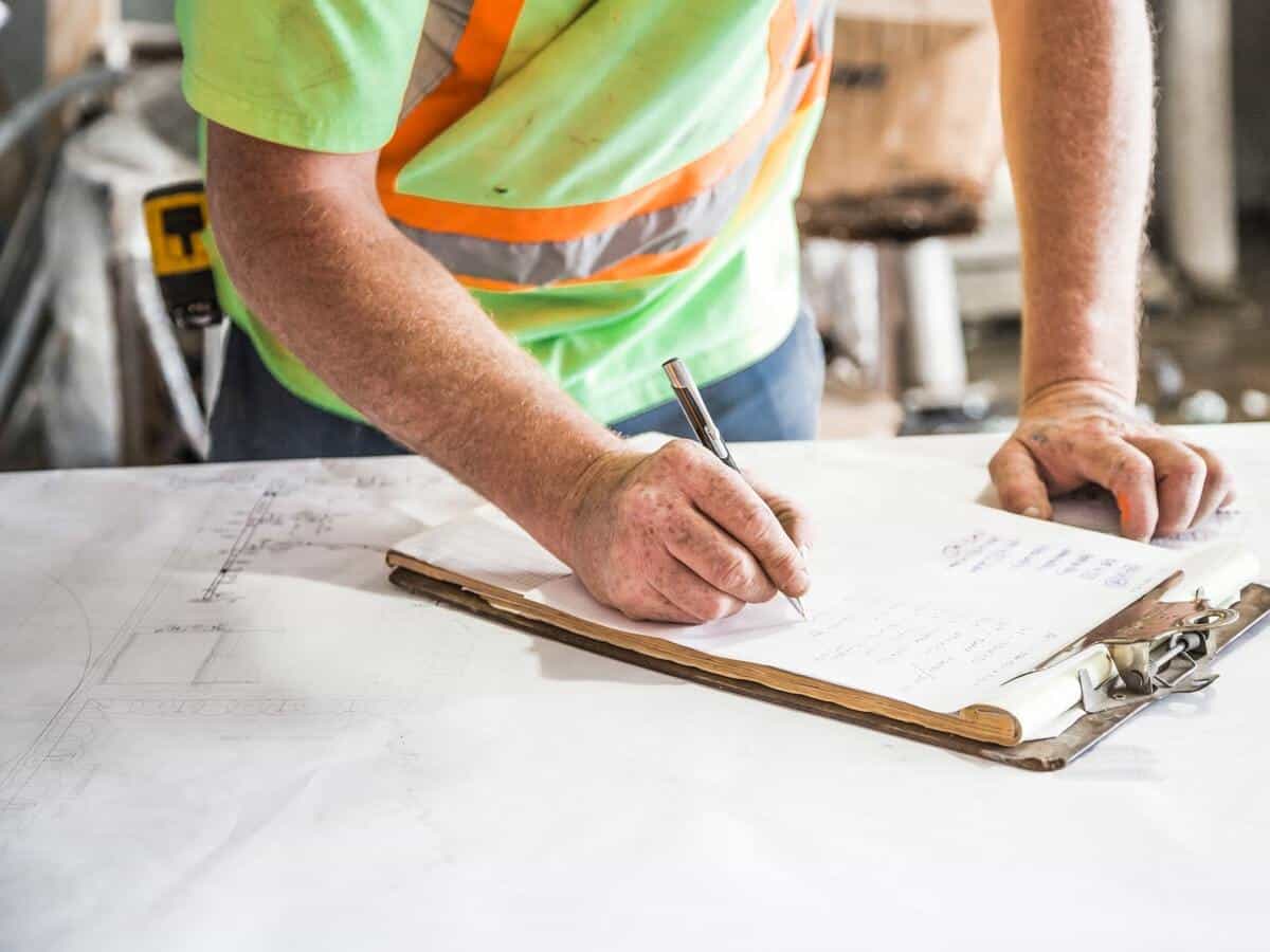 A roofing and construction worker filling out a tracking sheet that’s on top of a clipboard on a table.