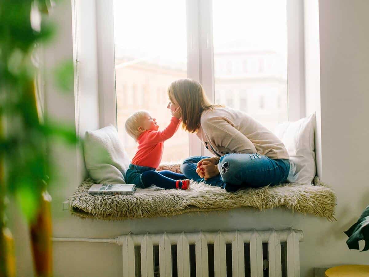 A baby pulls her mother's face towards her as they sit in a nook within their home.