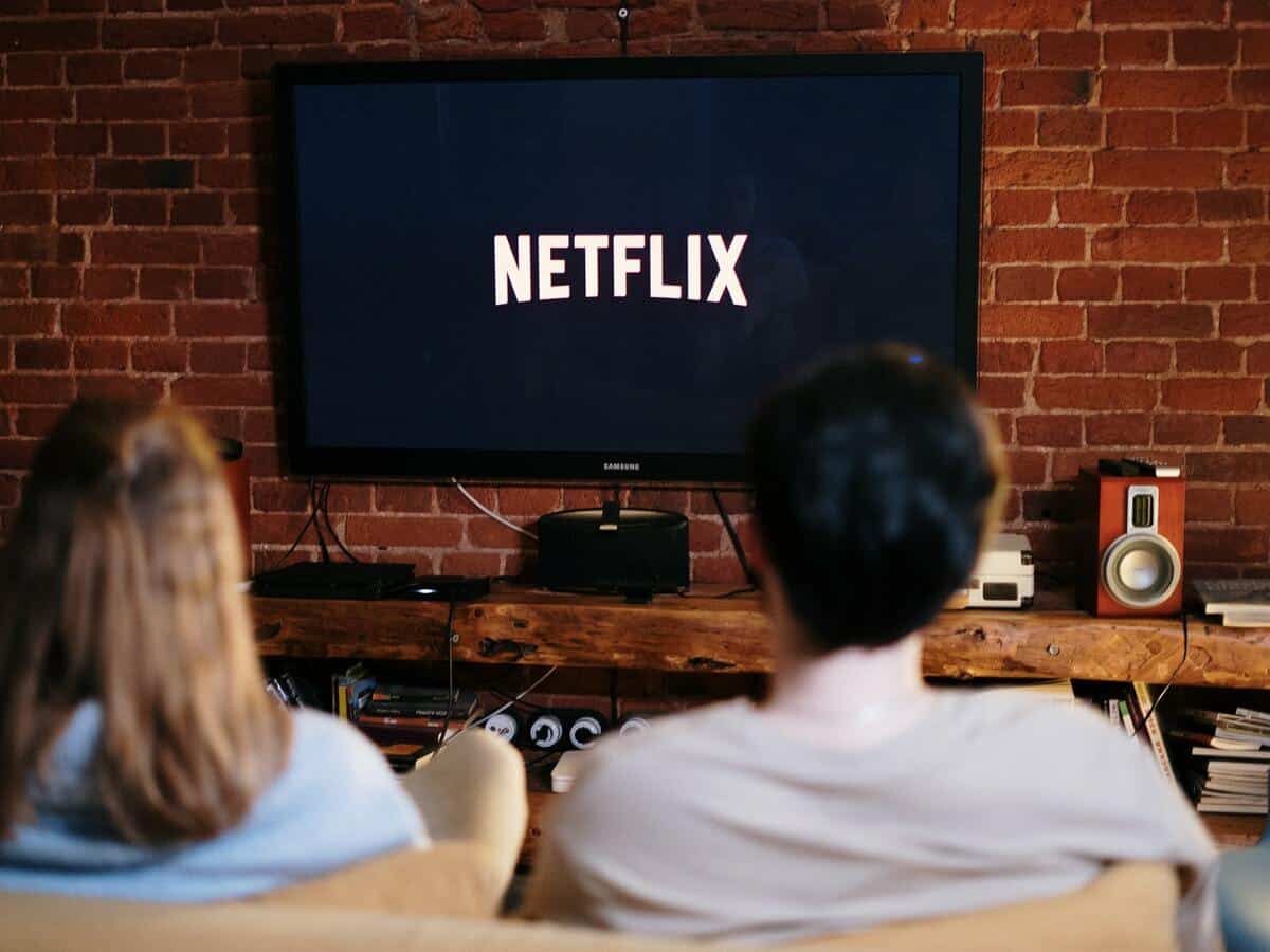 An over-the-shoulder view of a man and woman sitting on a couch, watching tv with Netflix on the screen.