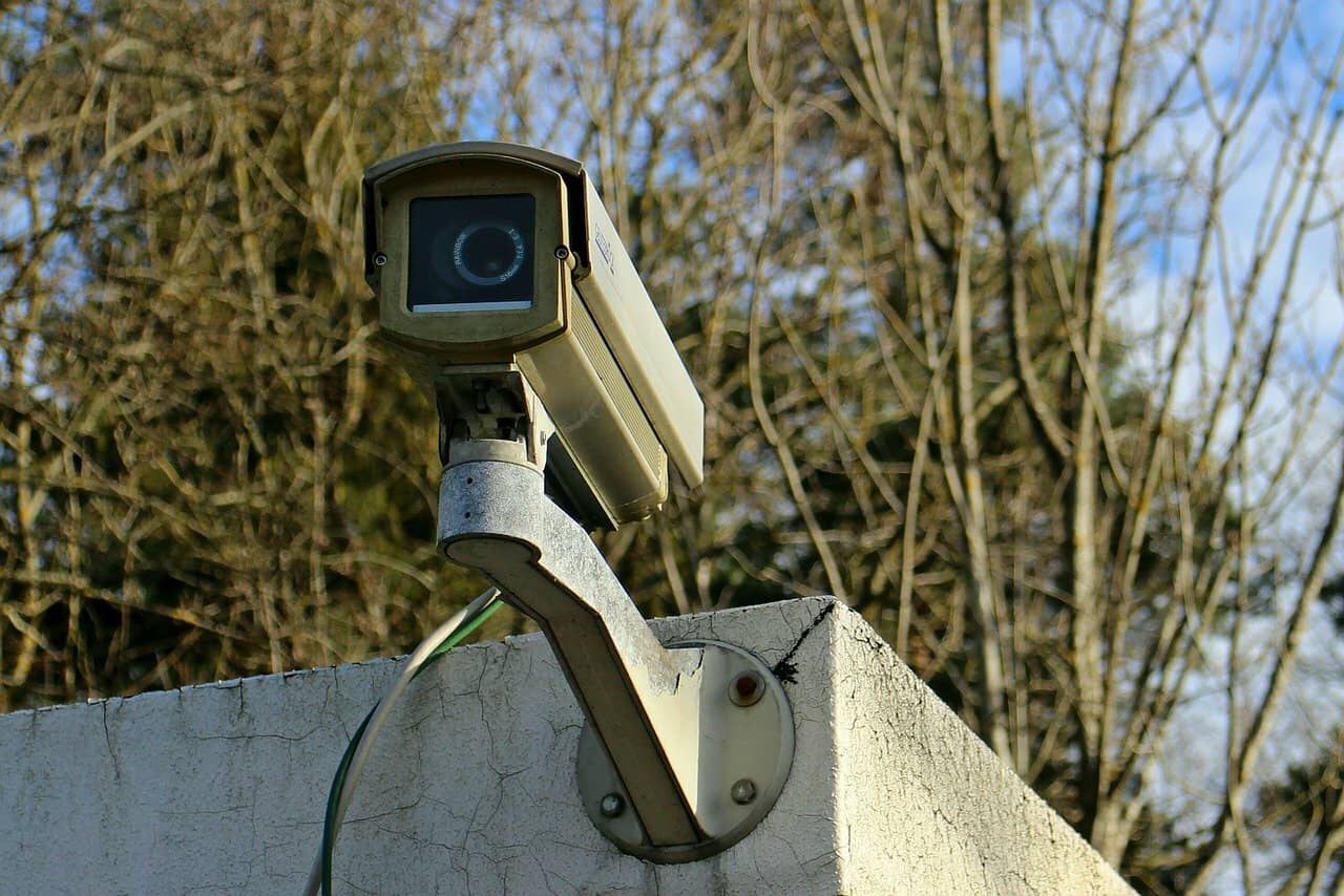 An outdoor security camera installed on a cement building that sits in front of trees.