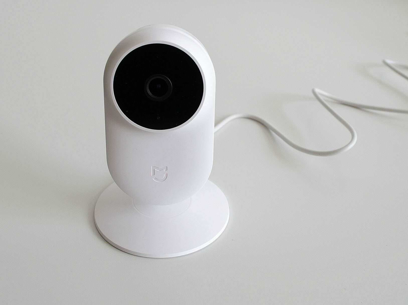 A white, modern security camera on top of a grey surface with a wire behind it.