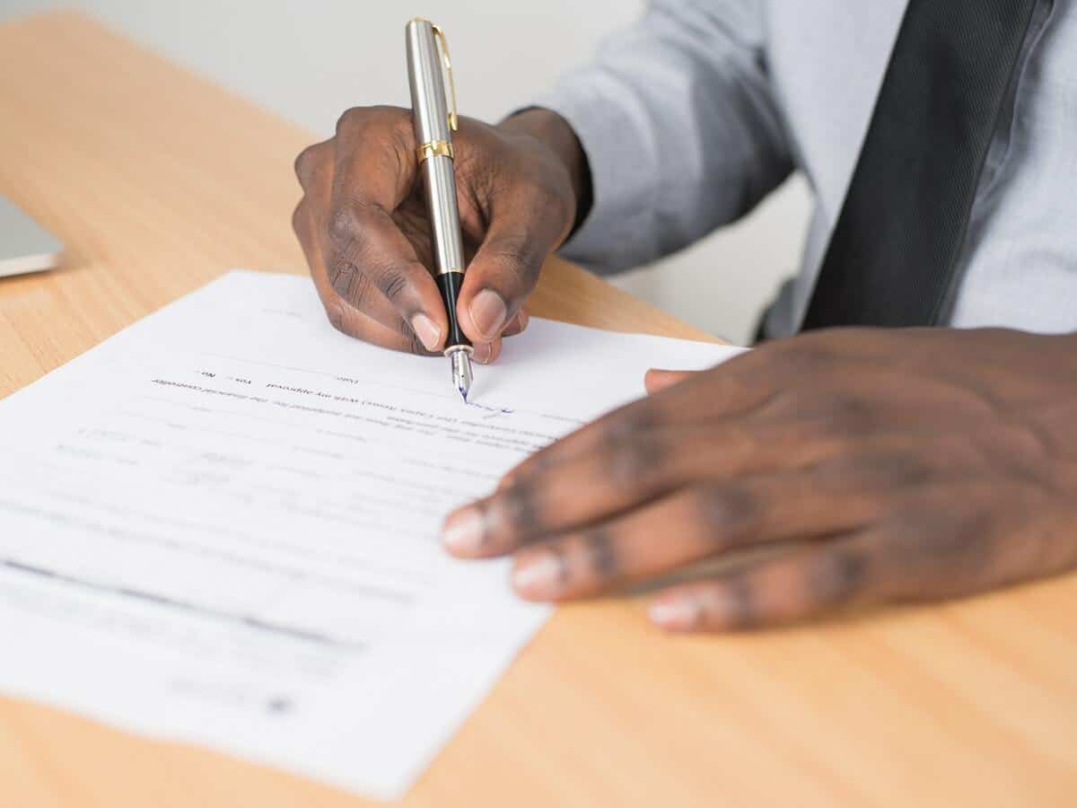 A man is signing a contract that's placed on a brown wooden table.