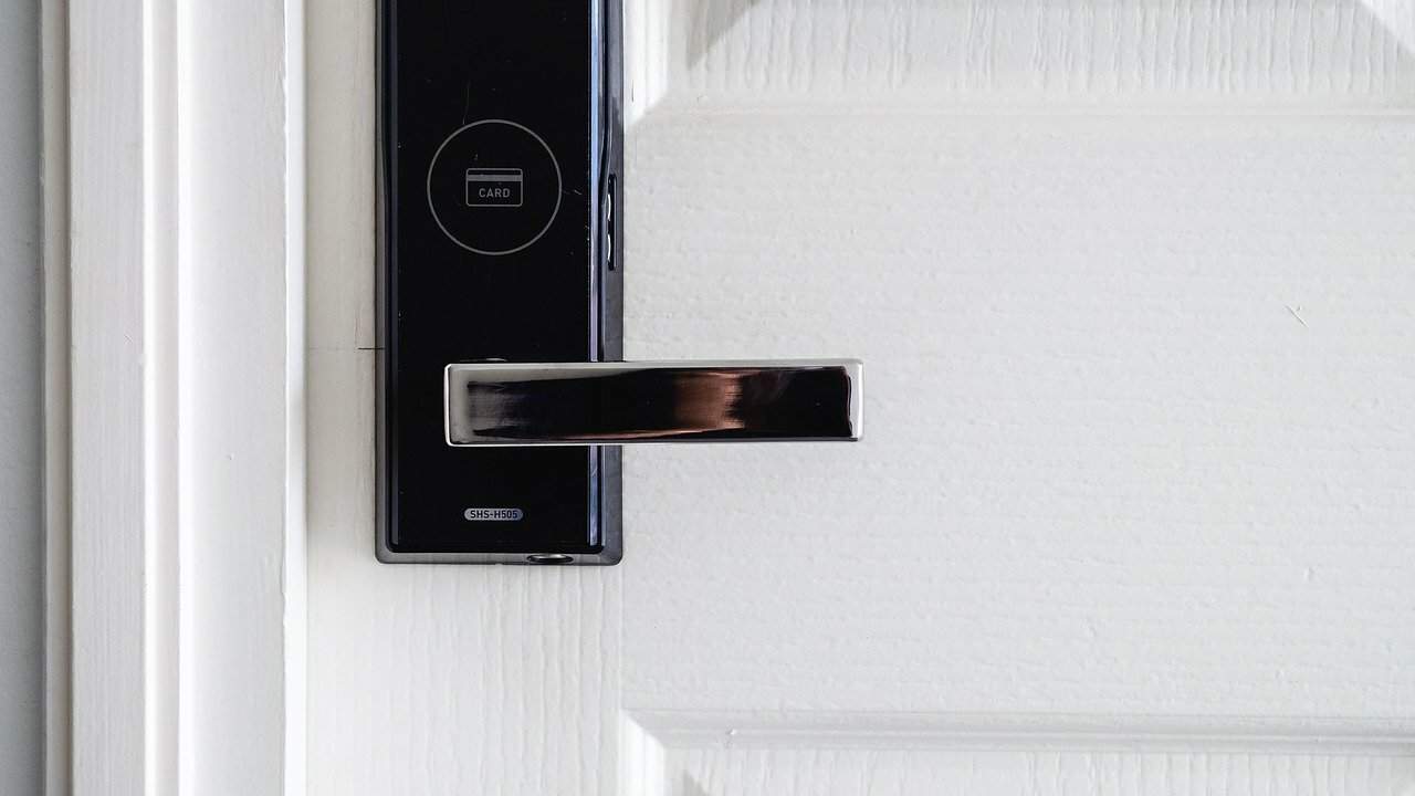 A professional home security system's smart door lock is installed on a white door.