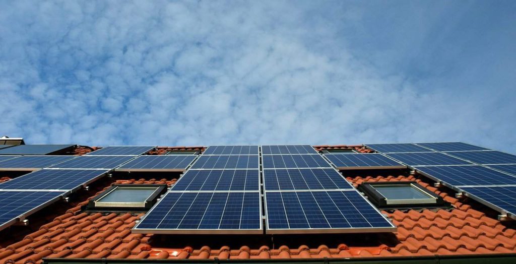 A view of a Spanish style roof with solar panels and the sky above it.