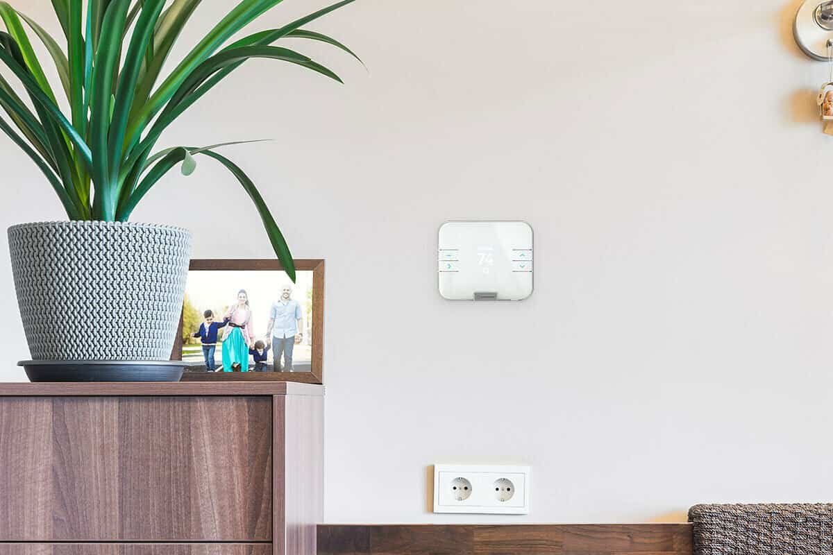 A smart thermostat is hanging on a beige wall inside a living room.