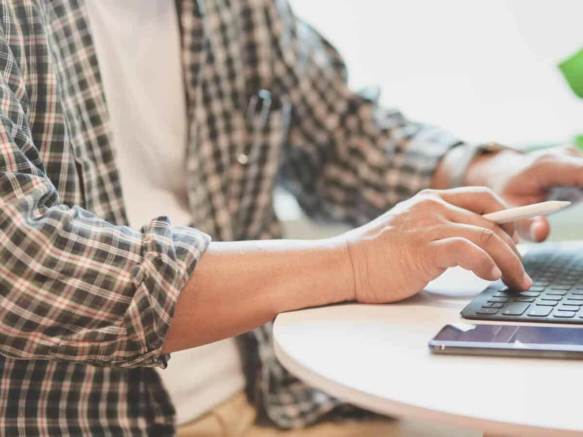 A man in a flannel shirt is working at a table on his computer.