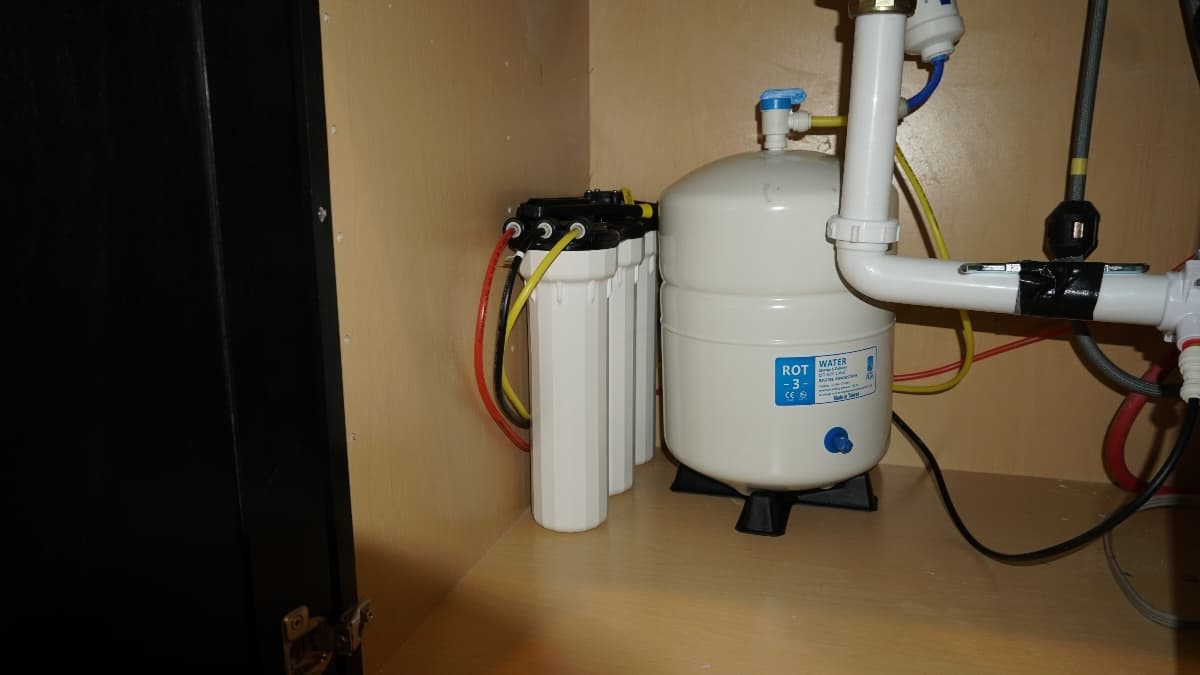 A whole home water filtration system installed under a kitchen sink.
