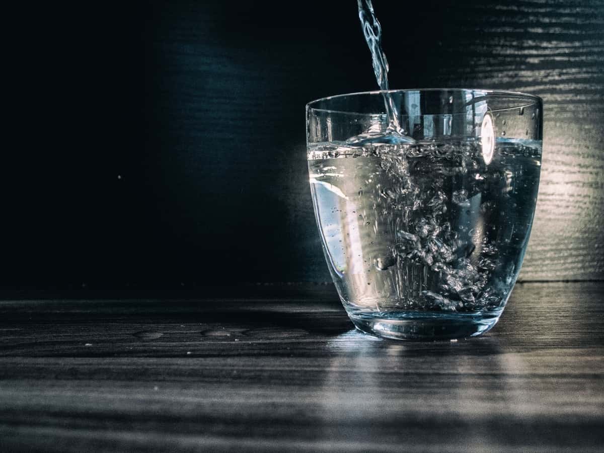 Water pouring into a modern, glass cup sitting on a dark wooden surface.