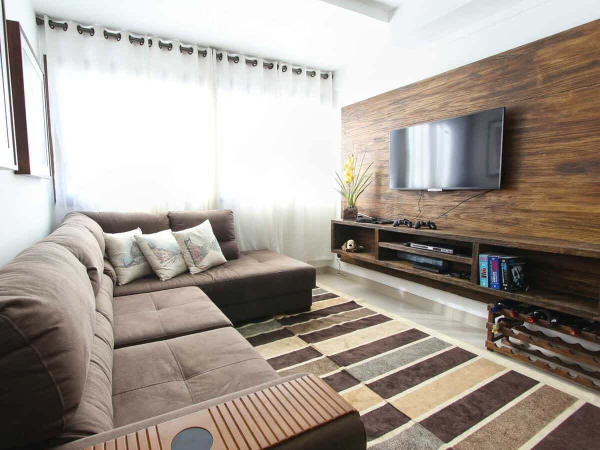 A modern living room with a brown sofa and a brown wooden paneled accent wall holding a flat screen television.