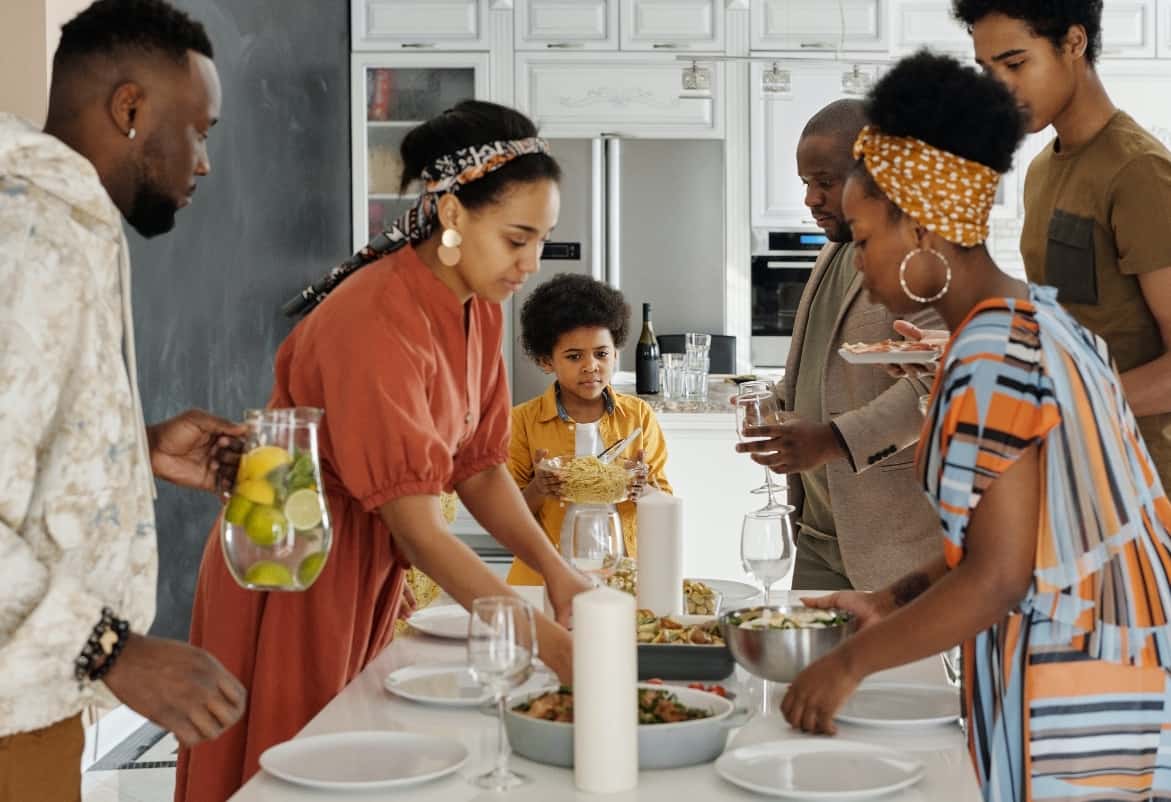 A family sets the kitchen table with food, plates and a pitcher of infused water for dinner.