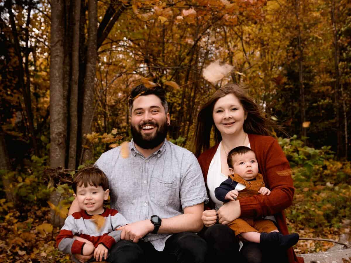 A mother and father sit with their sons outside in a fall setting.