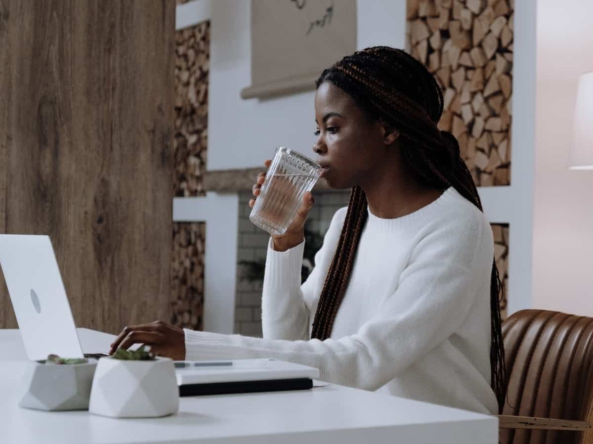 woman drinking water while on her laptop in white shirt