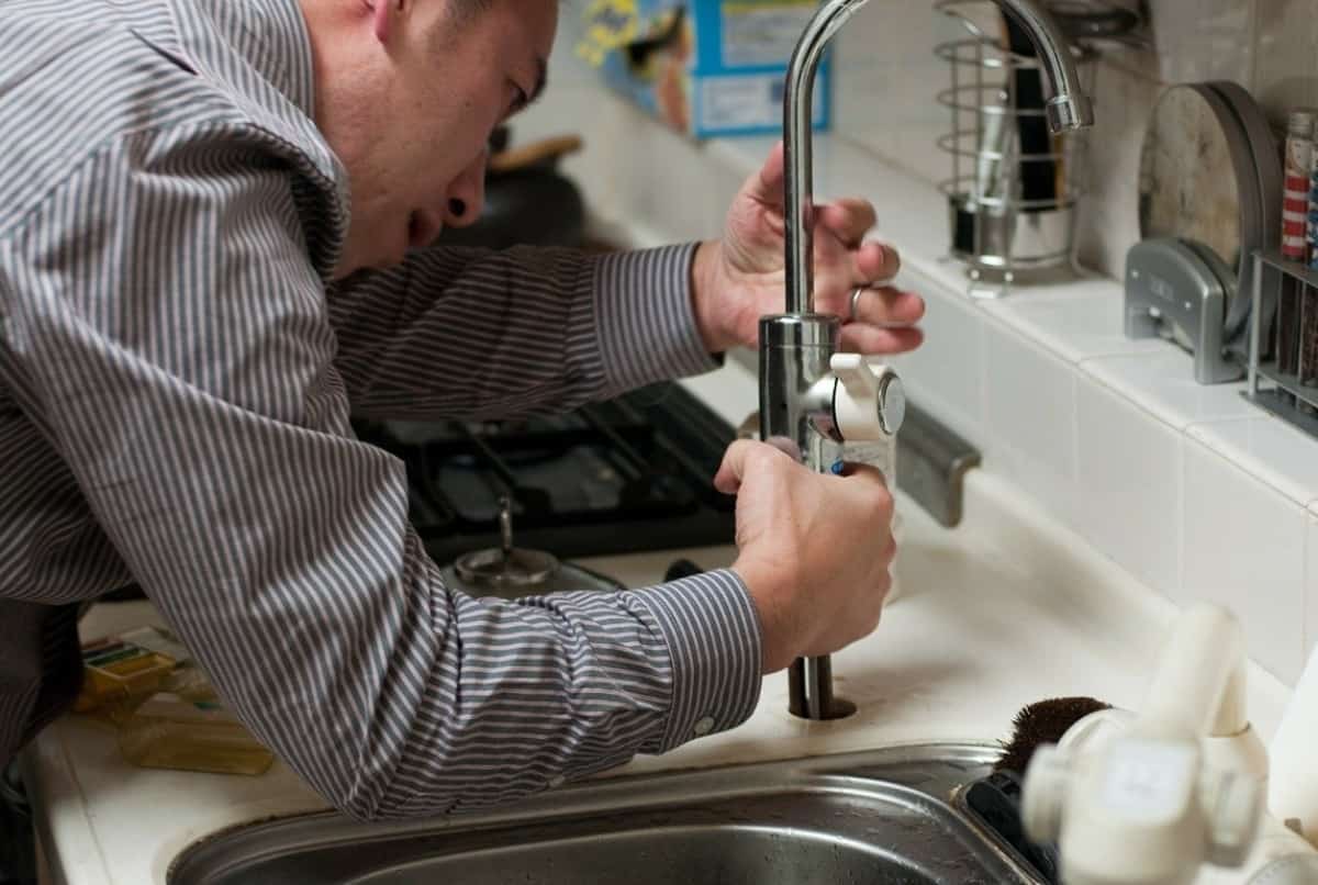 A home inspector is inspecting a kitchen faucet inside of a home.