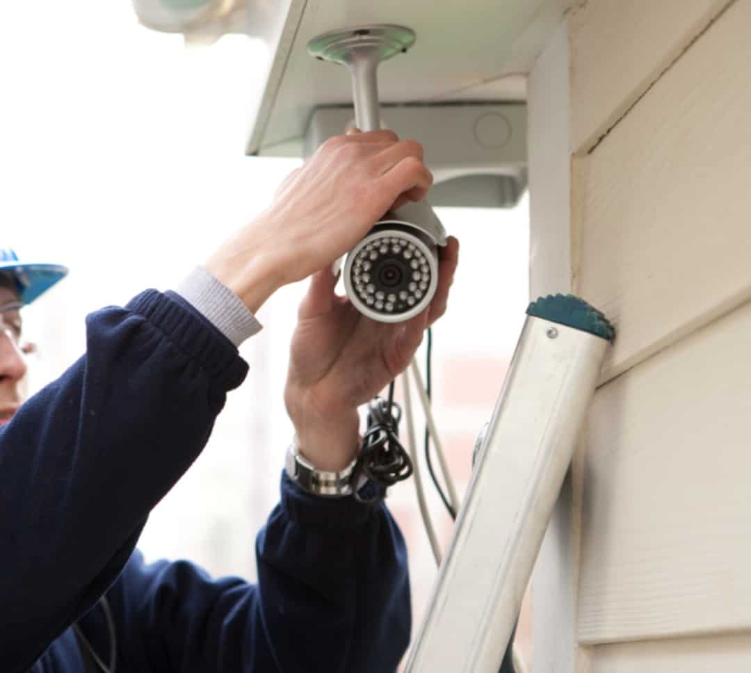 A professional home security installer places an outdoor security camera outside of a home.