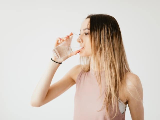 girl in pink shirt drinking water looking left