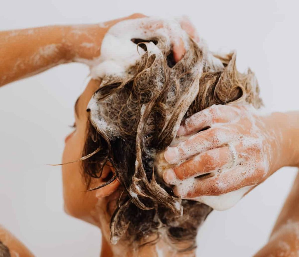 Soap suds in a woman's hair as she shampoos her strands.