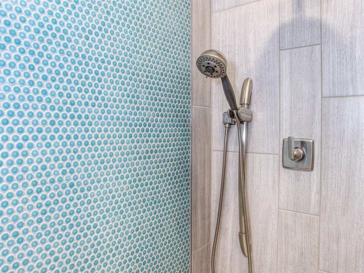 A silver showerhead inside of a bathroom shower with bright blue tiling on the wall.