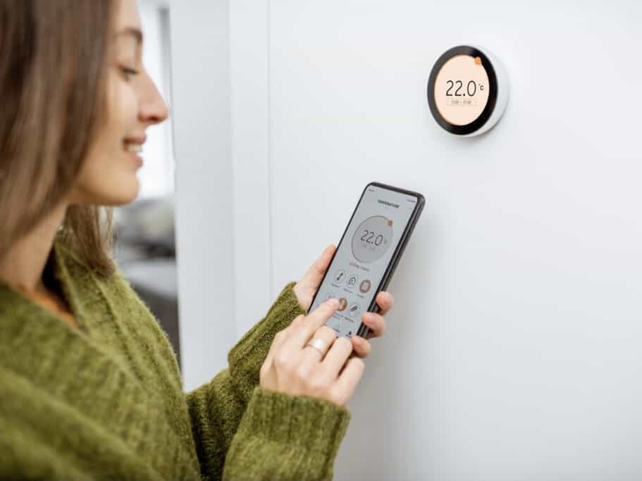 woman in green sweater adjusting thermostat through cell phone