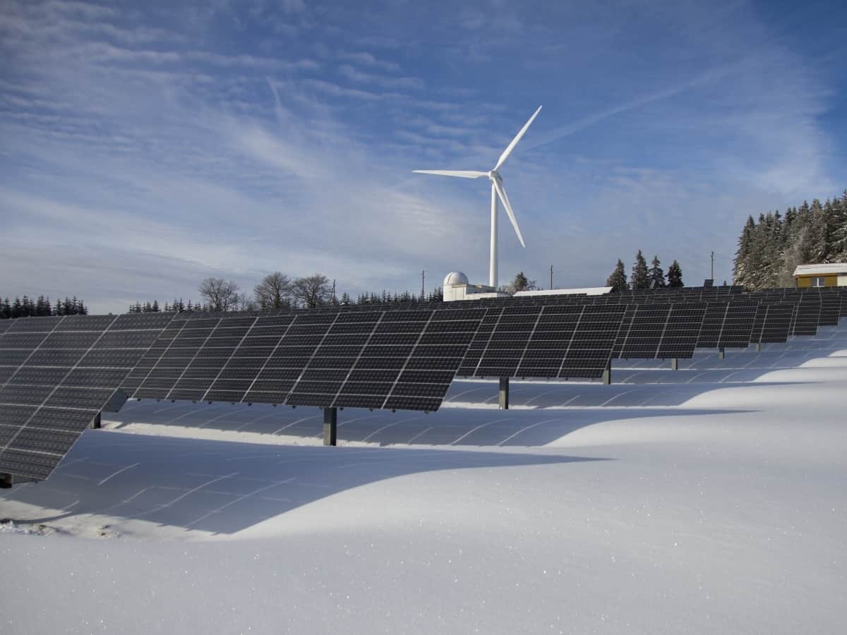 solar panels with wind energy in the background snow on ground and both renewable energy resources