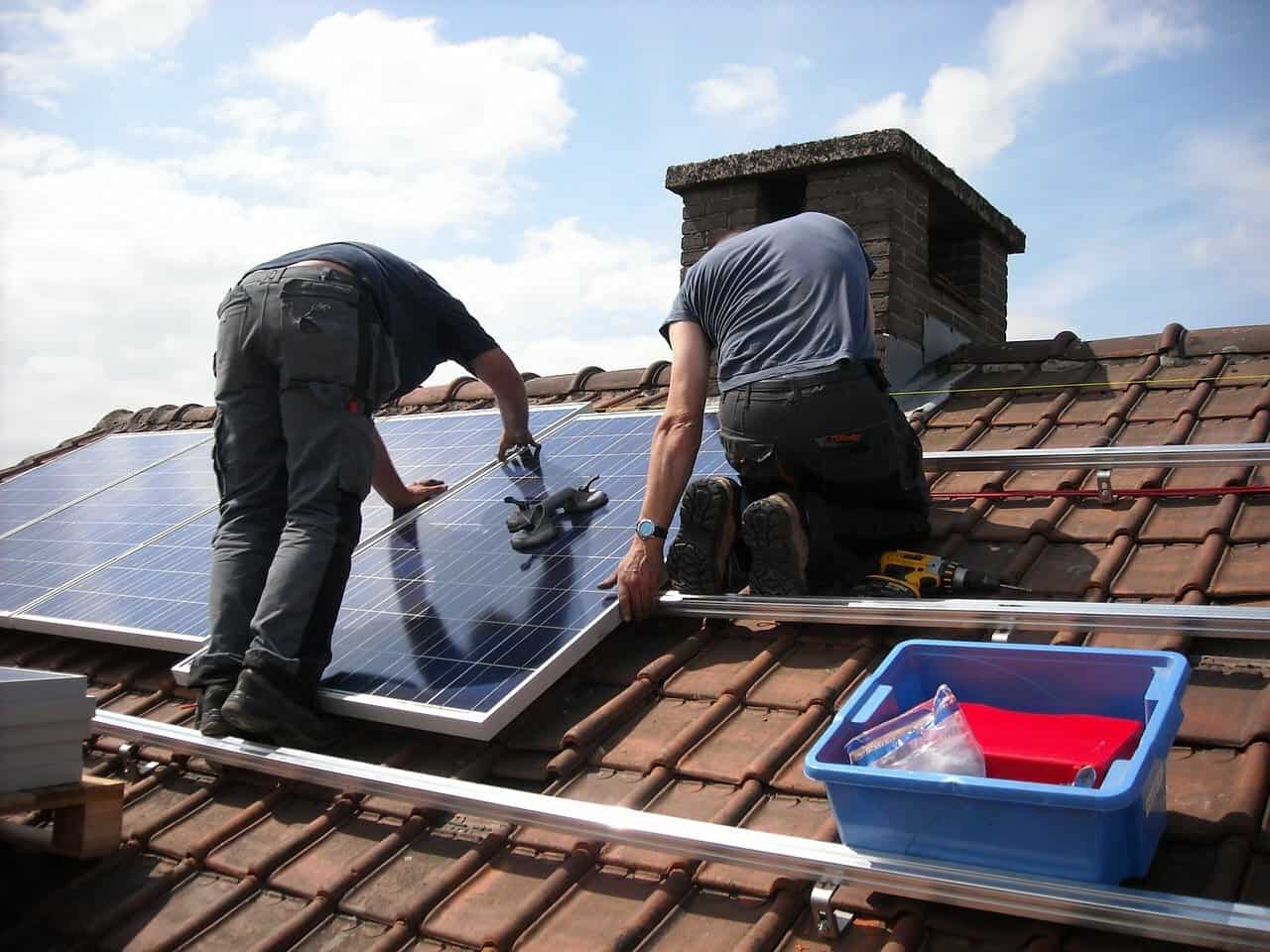 Two men are installing solar panels on the roof of a home with clay shingles.