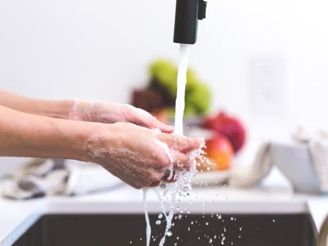 black faucet, person washing hands in sink, fruit in background