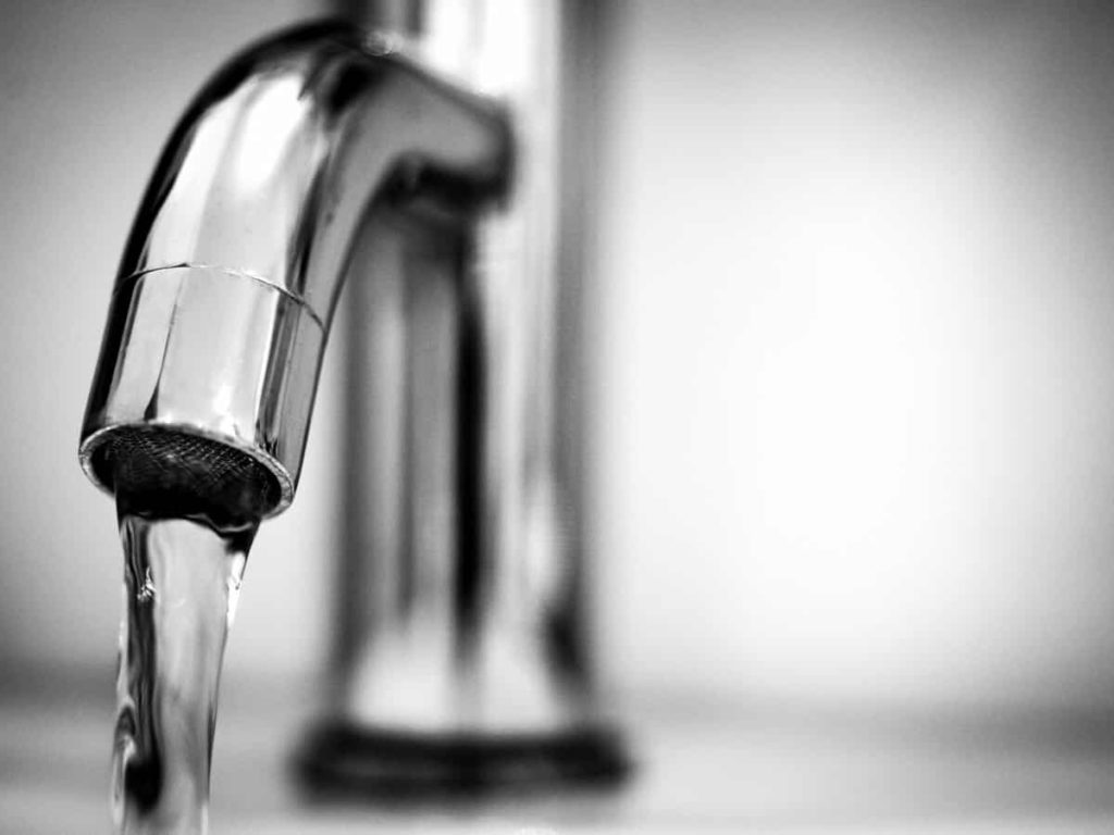 Water being released from a shiny silver faucet.