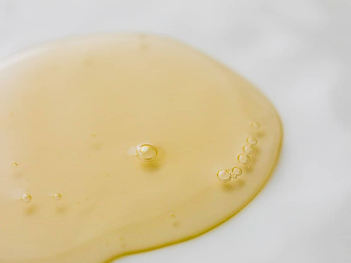 A puddle of creamy yellow shampoo is spread on a white granite surface.