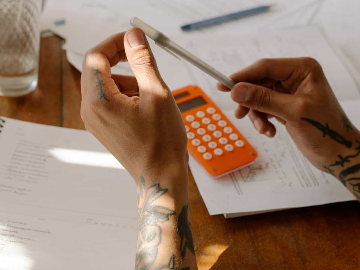 two hands, orange calculator, pen and paper