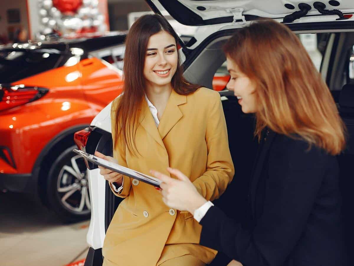 A woman speaks to a sales associate inside of a car dealership.