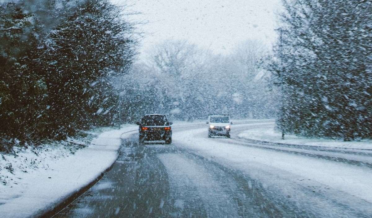 Two vehicles driving on opposite sides of the road as snow falls from the sky.