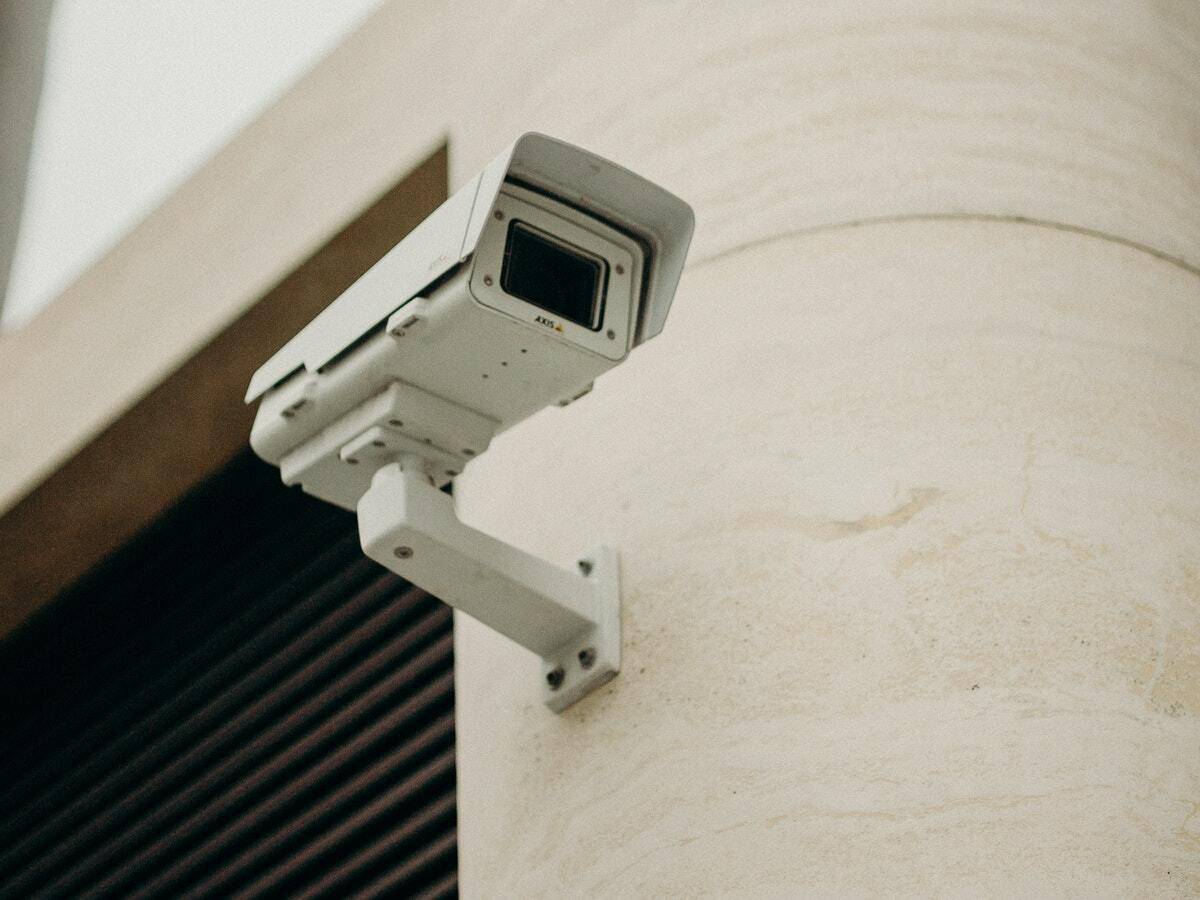 A white security camera installed on a modern, cement beige wall outside.
