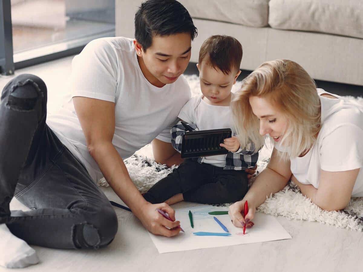 A man and woman coloring on the floor with their young child.
