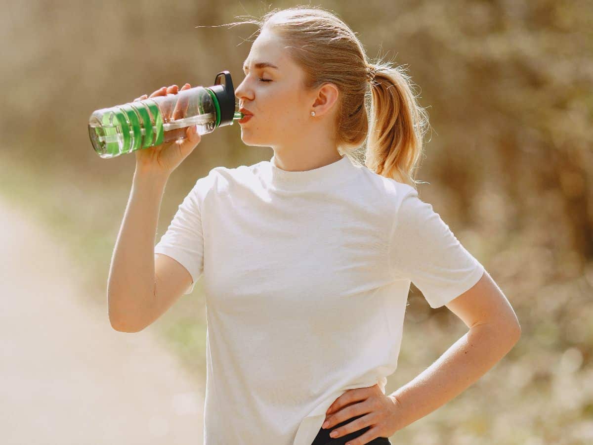 woman in white shirt with hand on hip stopping for a water break bottle