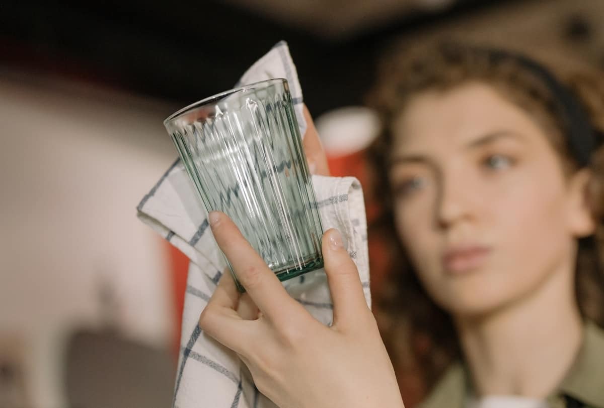 A woman is closely examining the glass she is cleaning with a towel.