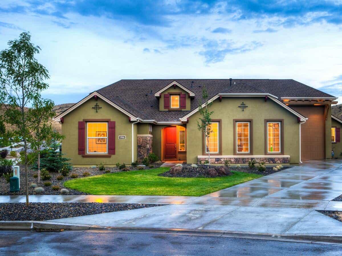 A one-story green stucco home with a sizable driveway.