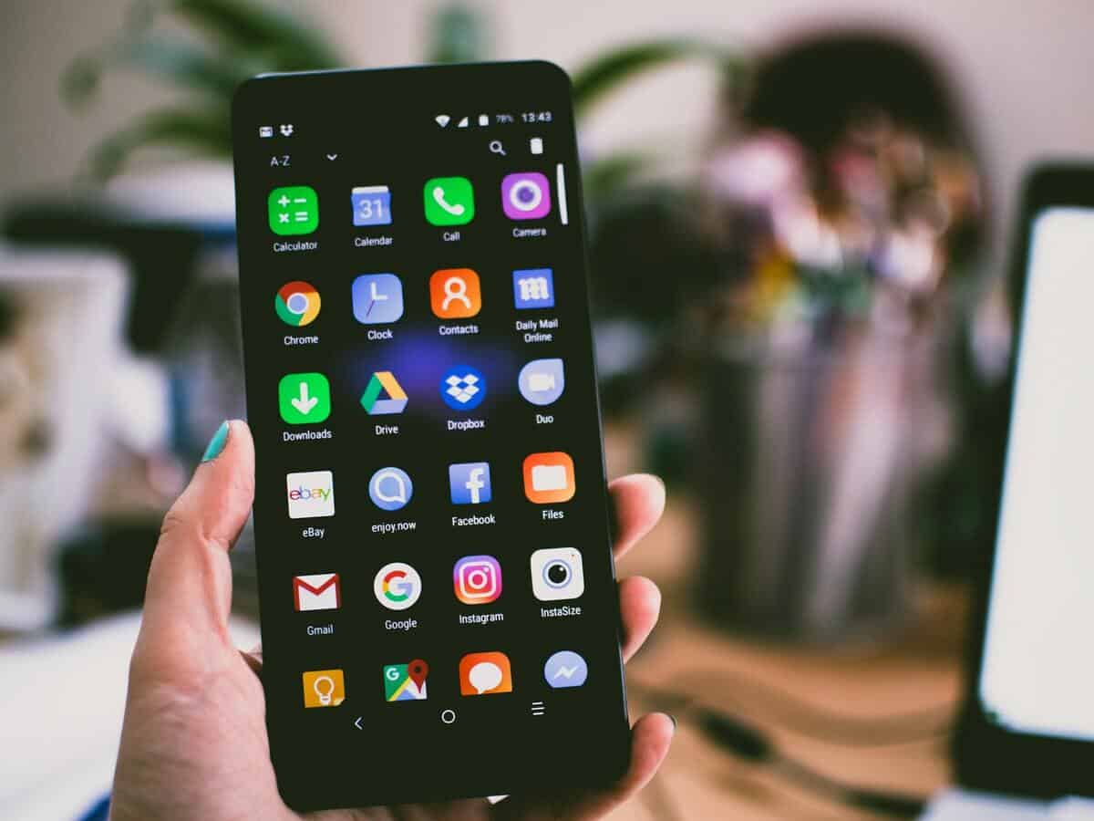 Closeup of a hand holding a black smartphone that’s opened to the home screen with rows of applications.