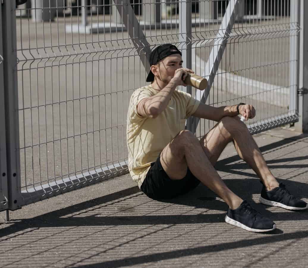 A young man sits outside while drinking from a filtered water bottle.