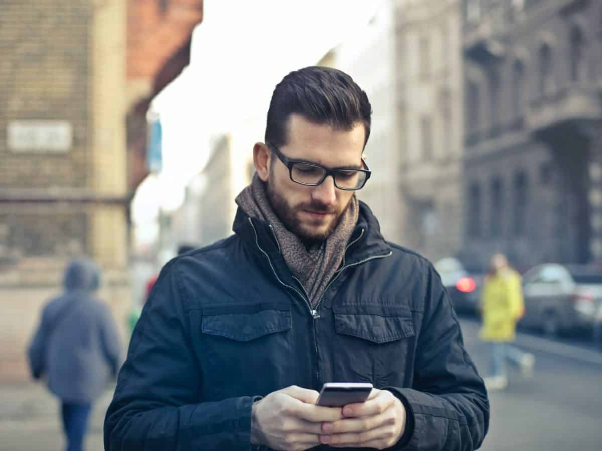 man in glasses looking down at phone while walking