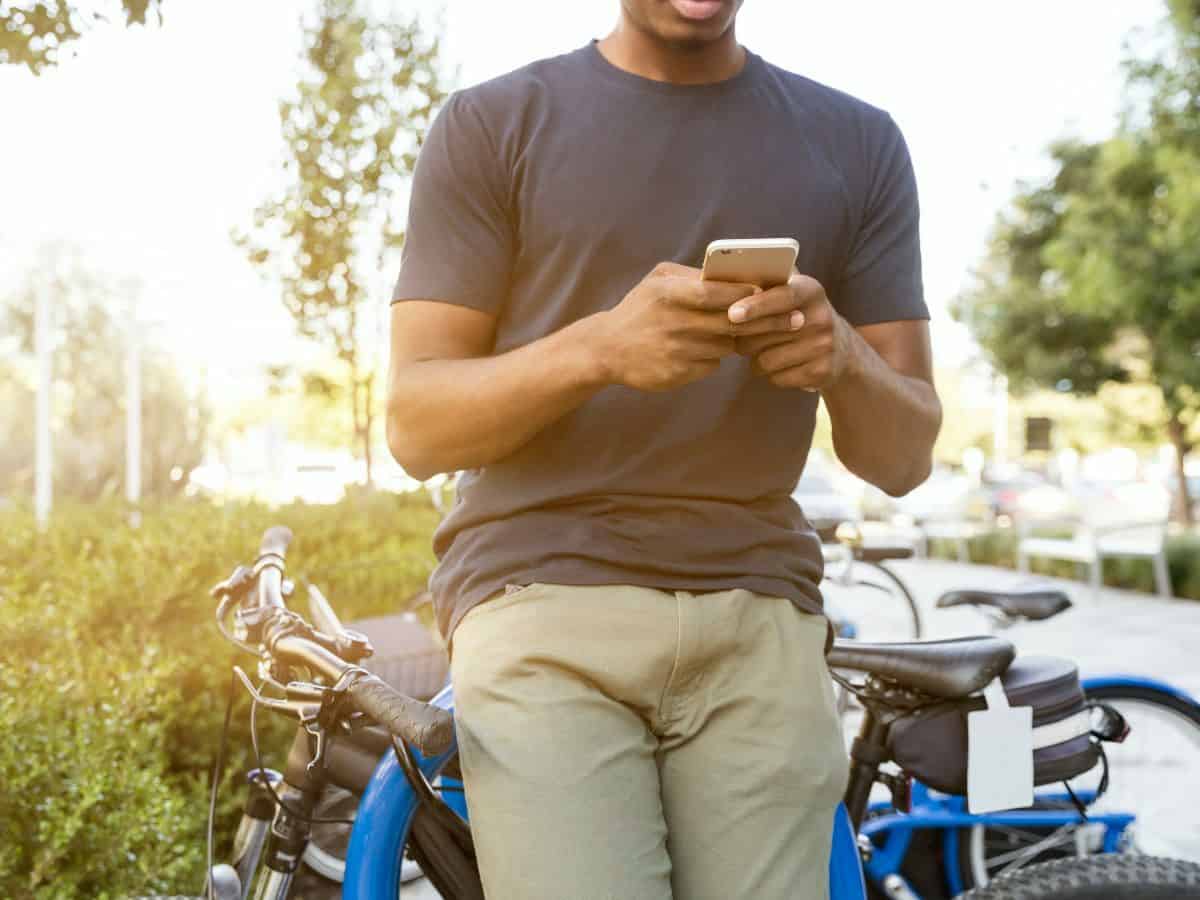 man looking at phone and leaning against bike 