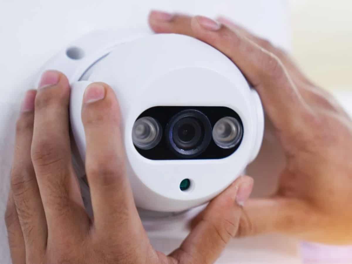 close up of two hands adjusting white security camera