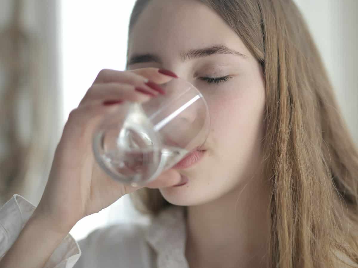 blonde drinking water out of clear glass straight on